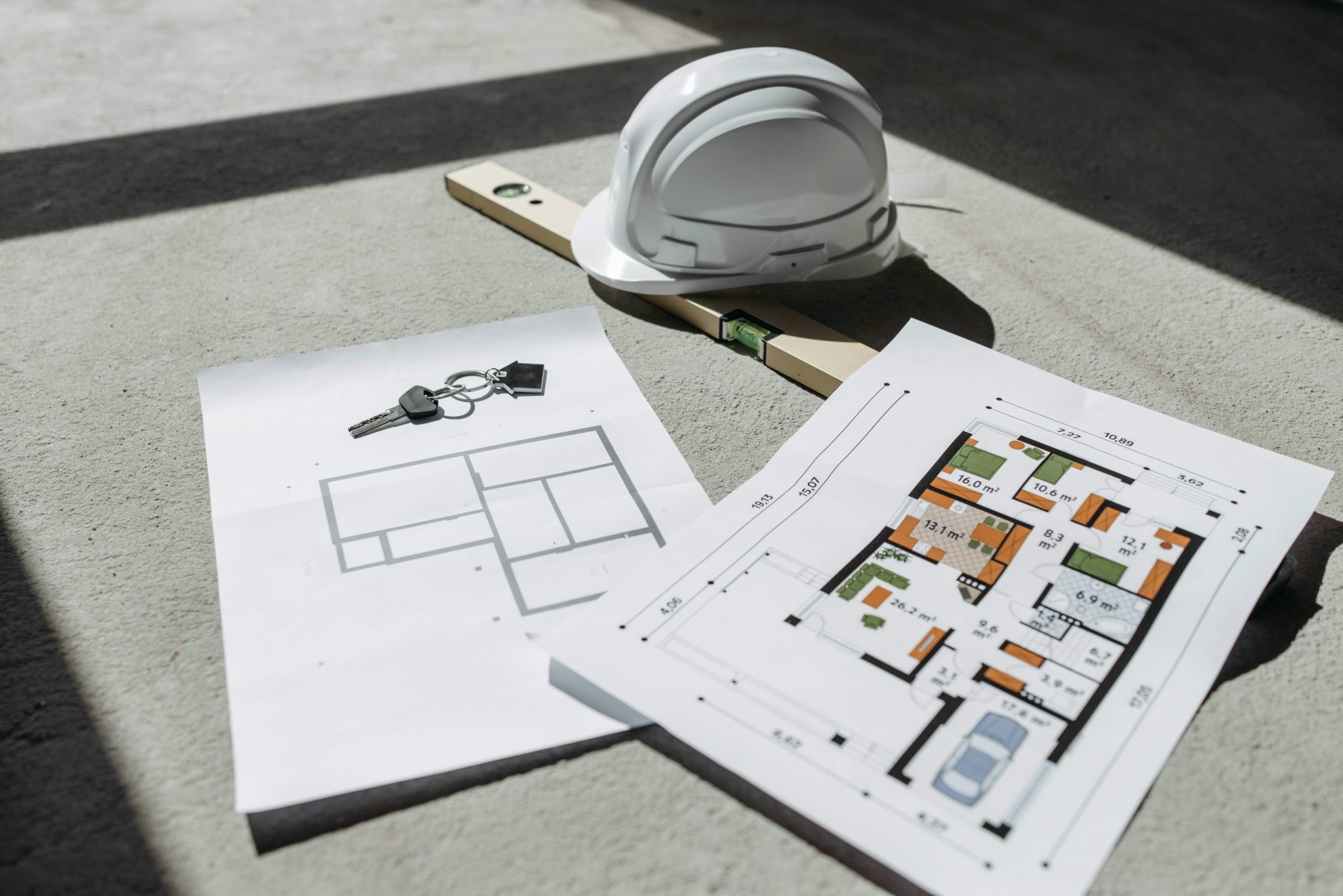 Métrage loi Carrez : plans d’appartement au sol avec casque de chantier, niveau à bulle et clés, préparation d’une vente en copropriété.
